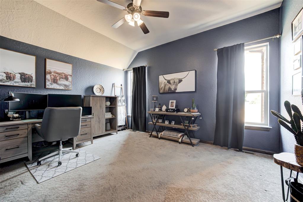 Furnished home office with vaulted ceiling, computer desk, cow artwork, and large curtained windows.
