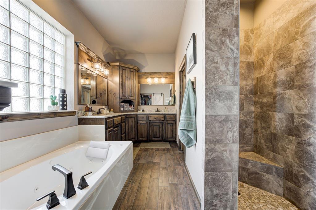 Bathroom with jetted tub, tiled walk-in shower, wood vanity, and glass-block window.