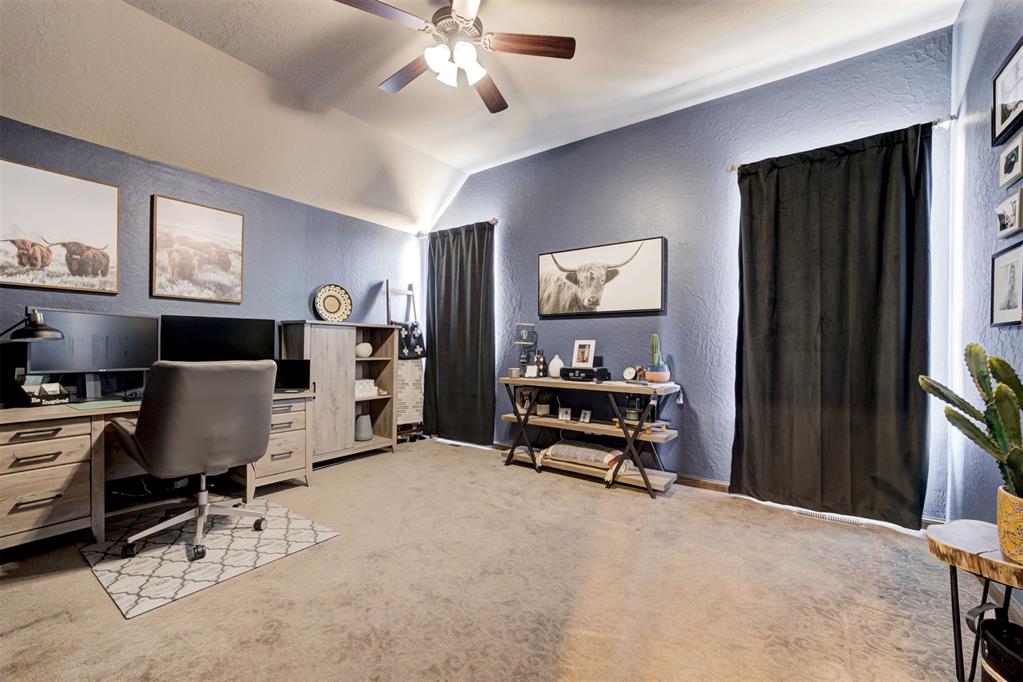 Furnished home office with a vaulted ceiling, computer desk, and black curtains.