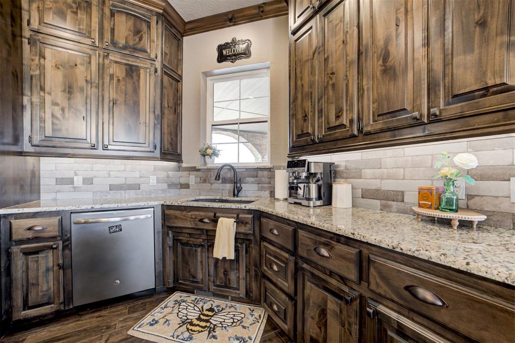 Kitchen with dark wood cabinets, granite counters, stone tile backsplash, and a window above the sink.