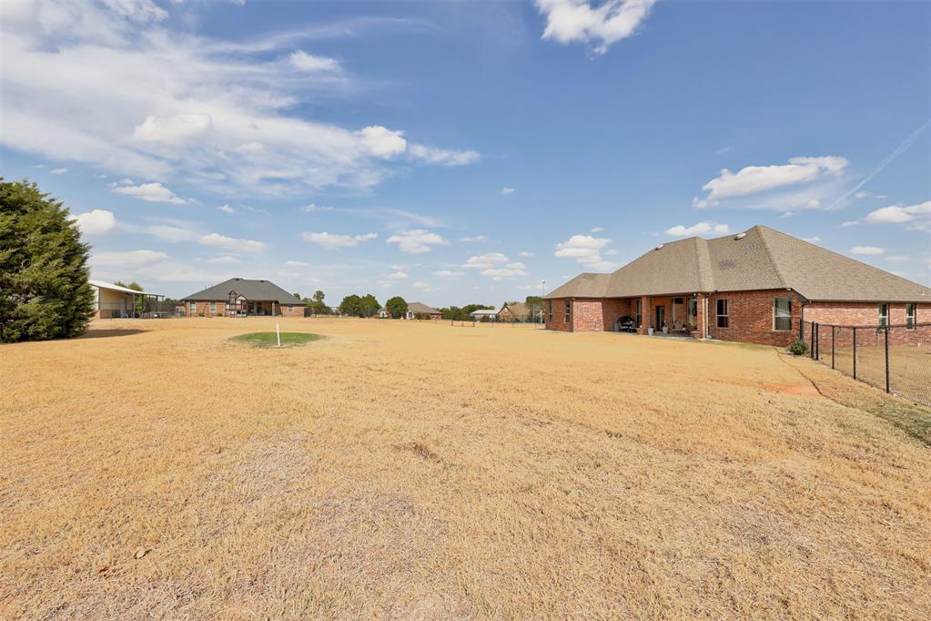 Brick home with a covered patio beside a wide, dry-grass backyard and black metal fence.