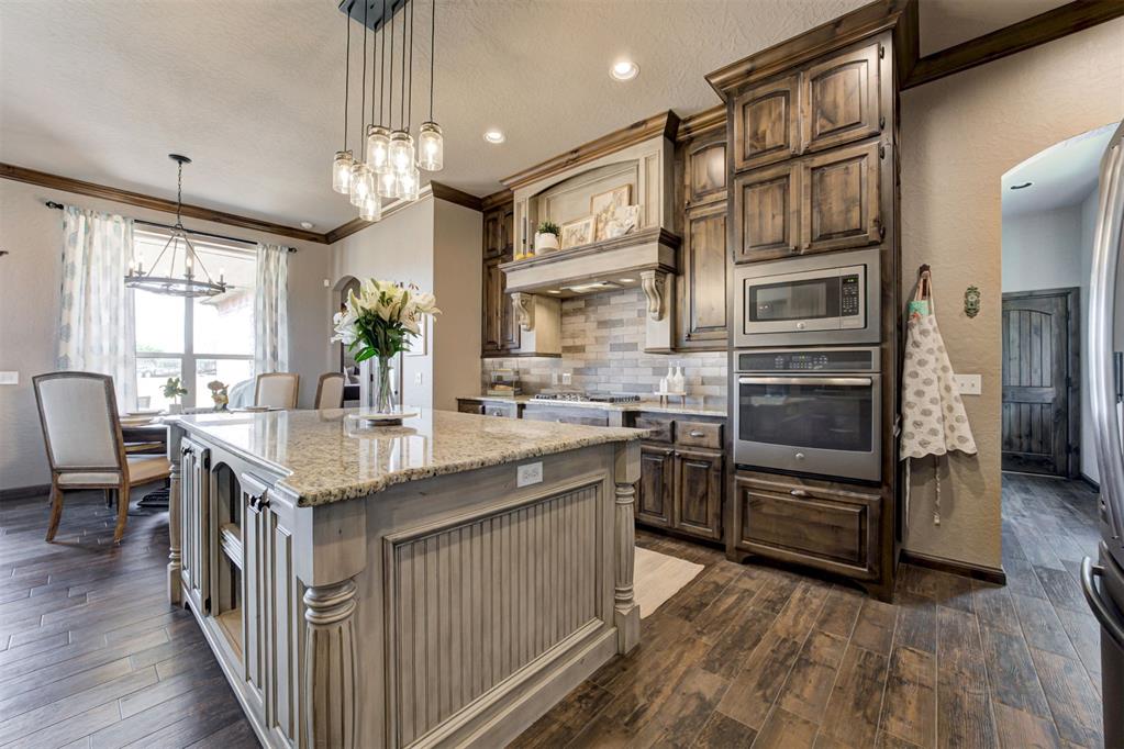 Kitchen with dark wood cabinets, stainless steel double ovens, and a large granite island.