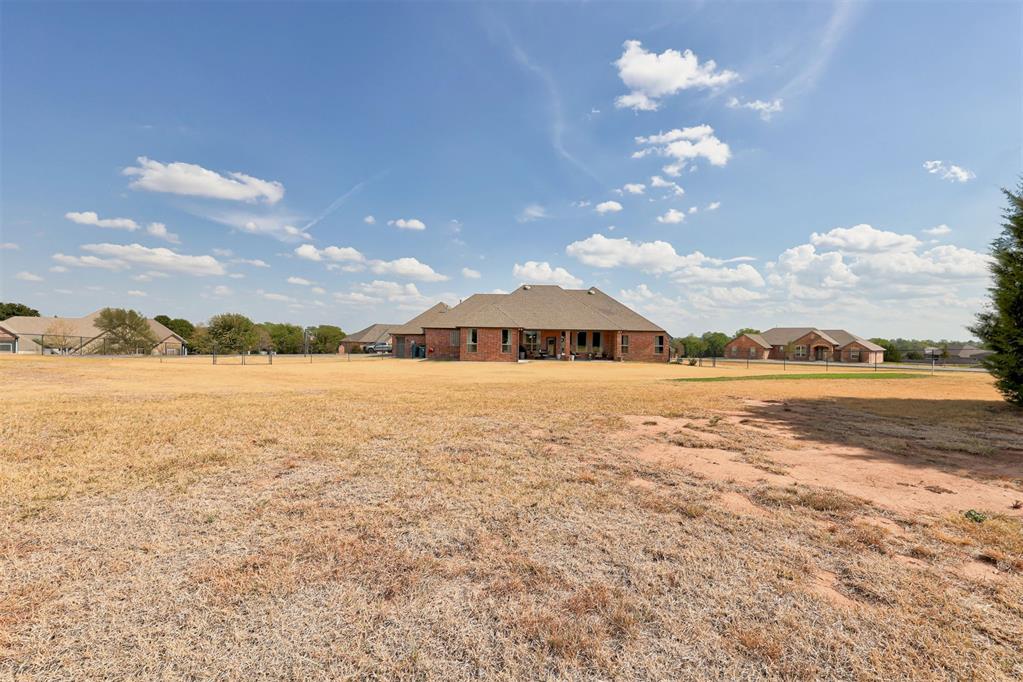 Single-story brick home with a covered back patio beyond a wide, dry lawn.