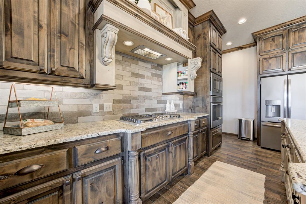 Kitchen with distressed wood cabinets, granite counters, a stone backsplash, and stainless steel appliances.