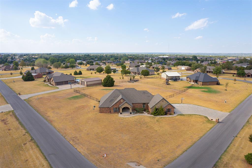 Aerial view of a brick home on a large corner lot, surrounded by a broad lawn and neighboring homes.