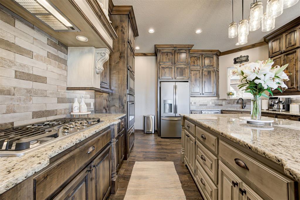 Kitchen with distressed-wood cabinetry, stone countertops, a large gas cooktop, and stainless steel refrigerator.