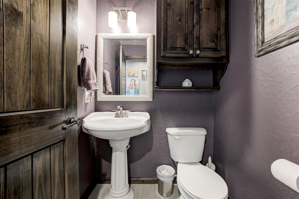 Bathroom with a white pedestal sink and toilet, dark wood cabinetry, and gray-purple walls.