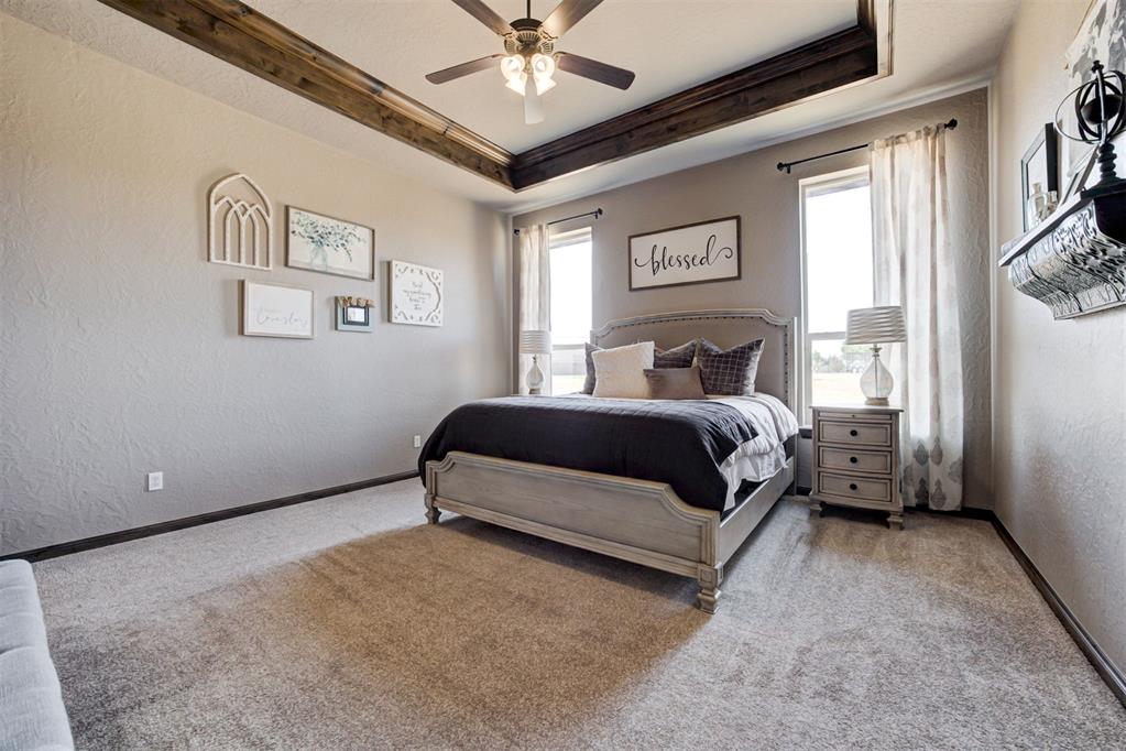 Bedroom with a gray bed, dark bedding, and a wood-trimmed tray ceiling with a ceiling fan.