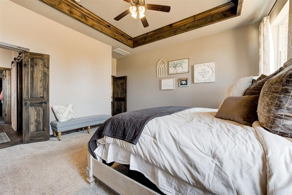 Bedroom with a white bed, dark quilt, wood-beamed tray ceiling, and cushioned bench.