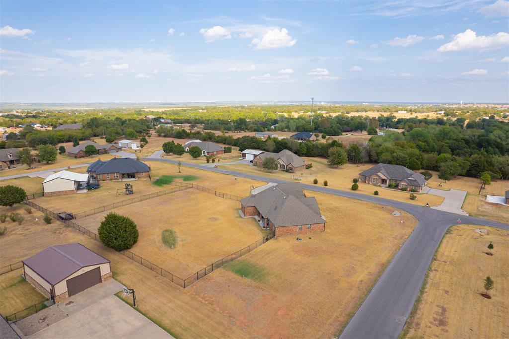 Aerial view of a brick home on a large fenced lot, with a detached garage and nearby homes.