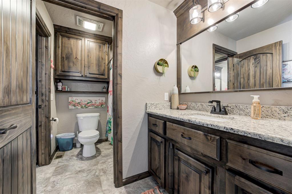 Bathroom vanity with granite countertop and dark wood cabinets beside a toilet alcove.
