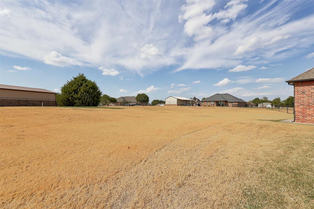 A broad dry grassy lot with buildings along the horizon beneath a cloudy sky.