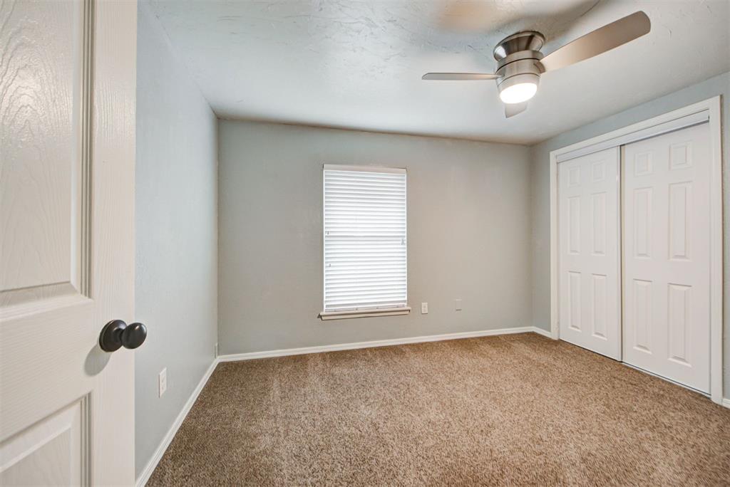 Empty bedroom with beige carpet, a window with blinds, sliding closet doors, and a ceiling fan.