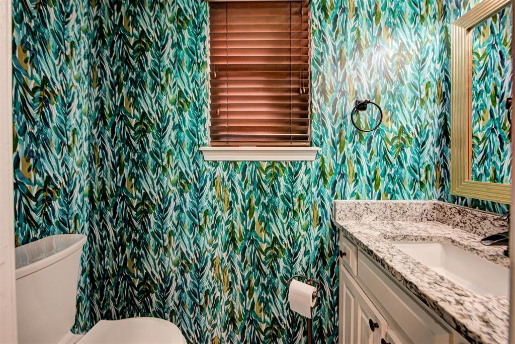Bathroom with leafy teal wallpaper, granite vanity, toilet, and window with wooden blinds.