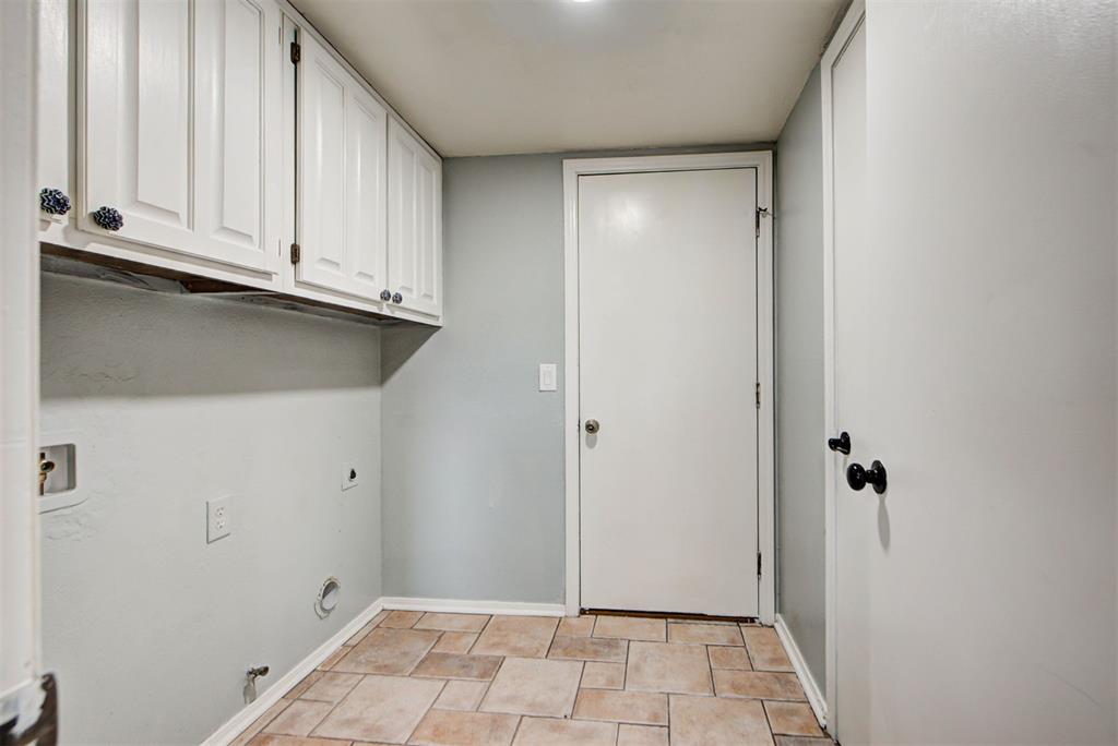 Empty laundry room with white cabinets, appliance hookups, and tan tile flooring.