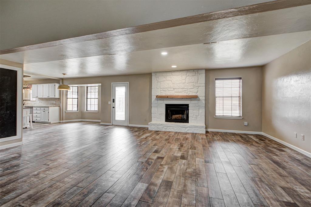 Vacant living room with a white stone fireplace, wood-look floors, and an open kitchen.