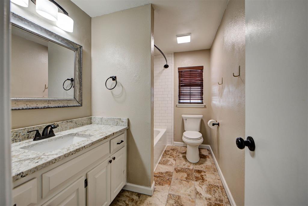 Bathroom with a stone-topped vanity, tiled floor, and window above the toilet.