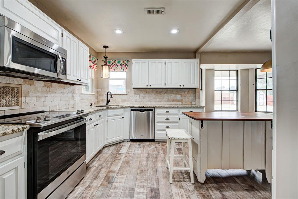 Kitchen with white cabinets, stainless appliances, stone backsplash, and a wood-topped peninsula.