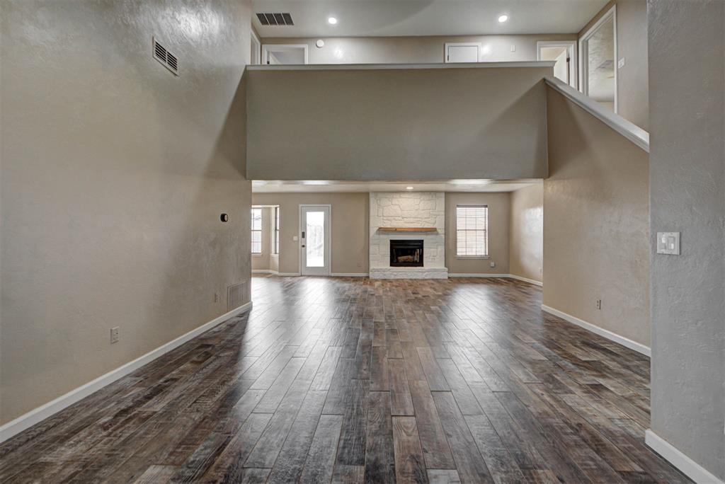 Vacant living room with a stone fireplace, dark plank flooring, and an open loft above.