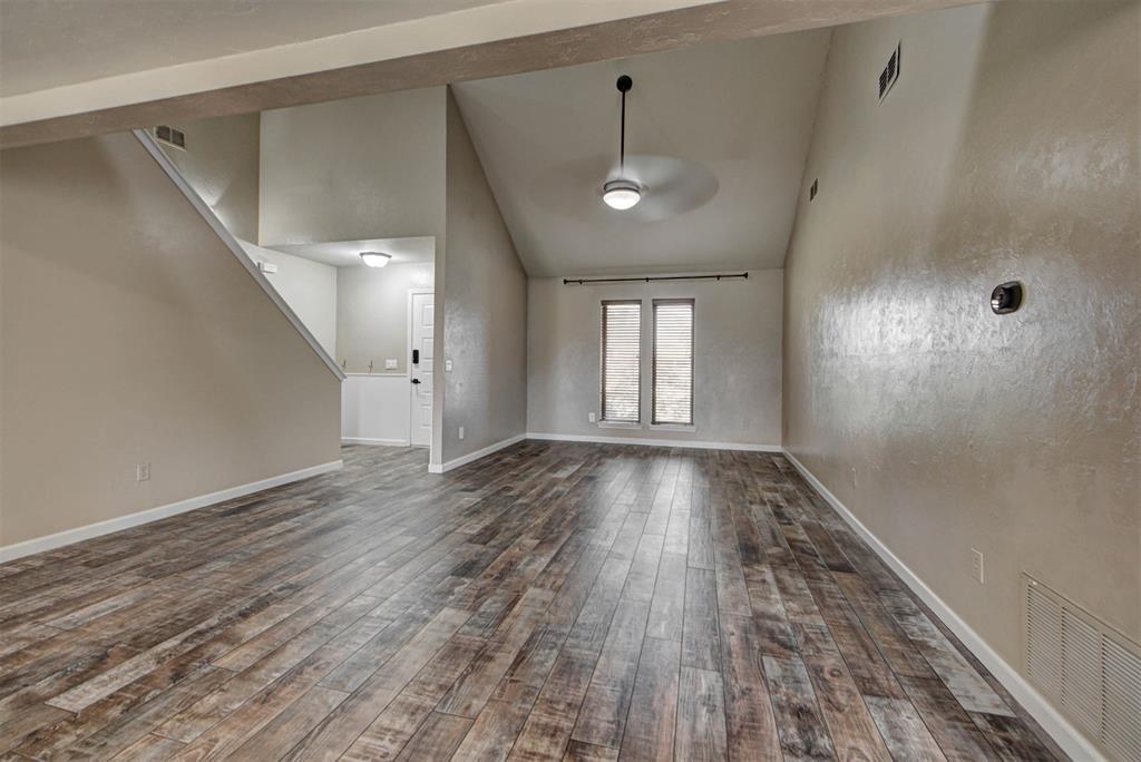 Empty living room with wood-look flooring, high ceiling, and two narrow windows.