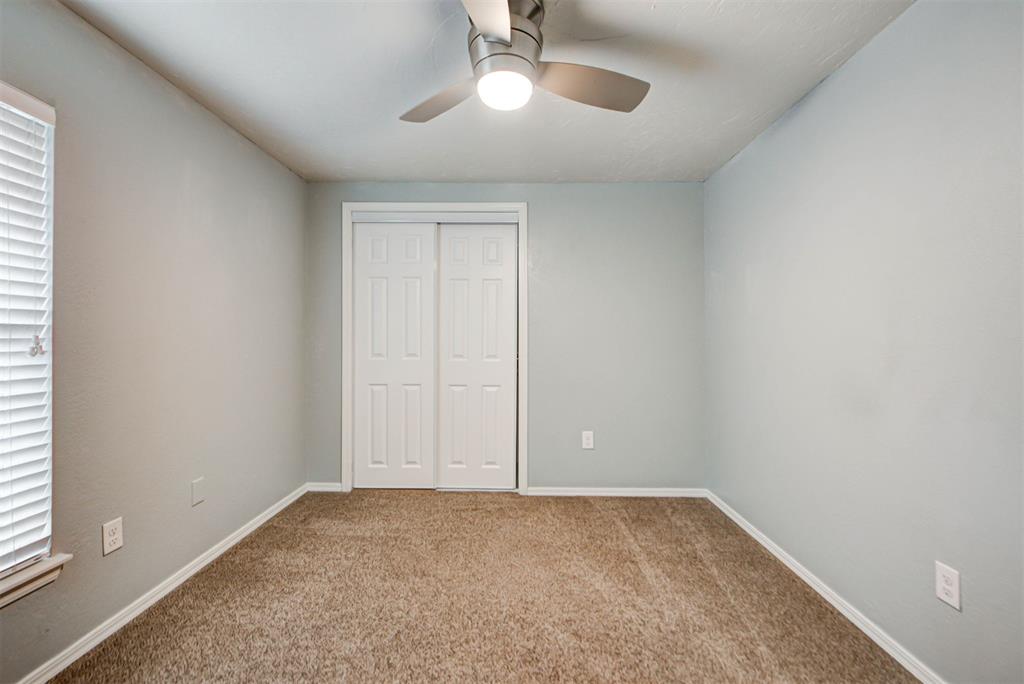 Empty bedroom with beige carpet, white double closet doors, and a ceiling fan with light.