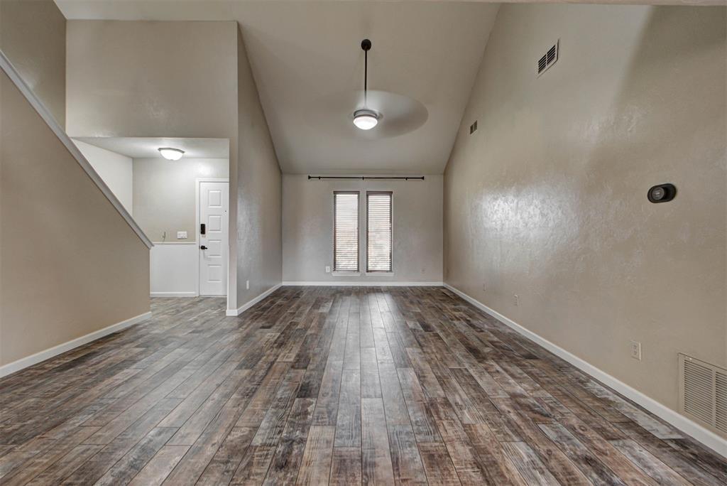 Empty living room with tall ceiling, ceiling fan, narrow windows, and wood-look flooring.