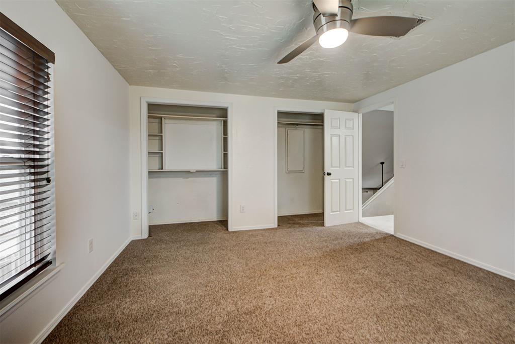 Empty bedroom with brown carpet, open closets, dark window blinds, and a ceiling fan.