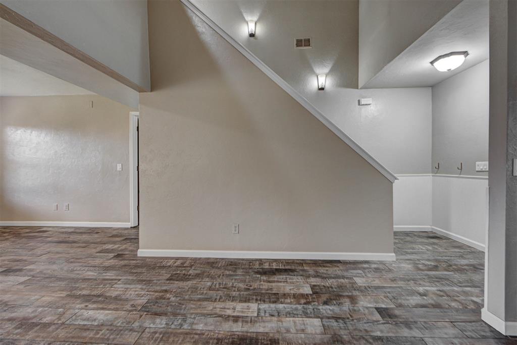 Empty interior with wood-look tile flooring and a large sloped wall beneath the staircase.