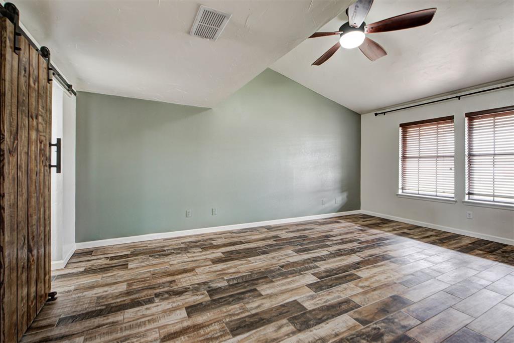 Empty room with wood-look tile flooring, a ceiling fan, two blinded windows, and a rustic sliding barn door.