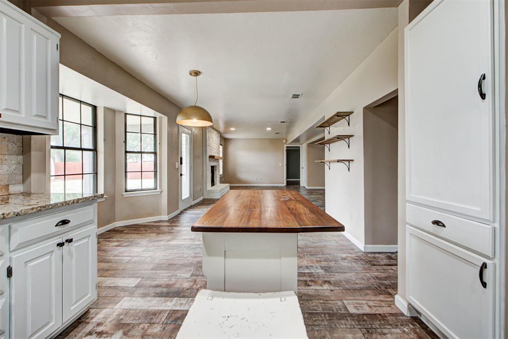 Kitchen with a large wood-topped island, white cabinets, open shelves, and tall windows.