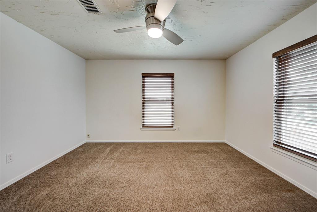 Empty carpeted room with a ceiling fan and two windows with blinds.
