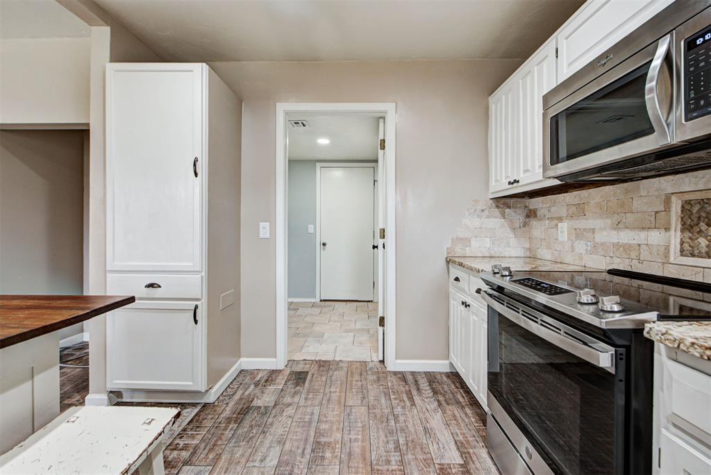 Kitchen with white cabinets, stainless steel appliances, stone backsplash, and wood-look flooring.
