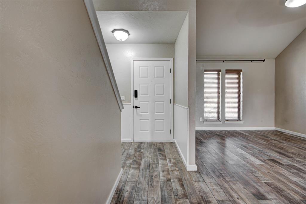 Entryway with a white paneled front door, plank flooring, and two narrow windows with blinds.