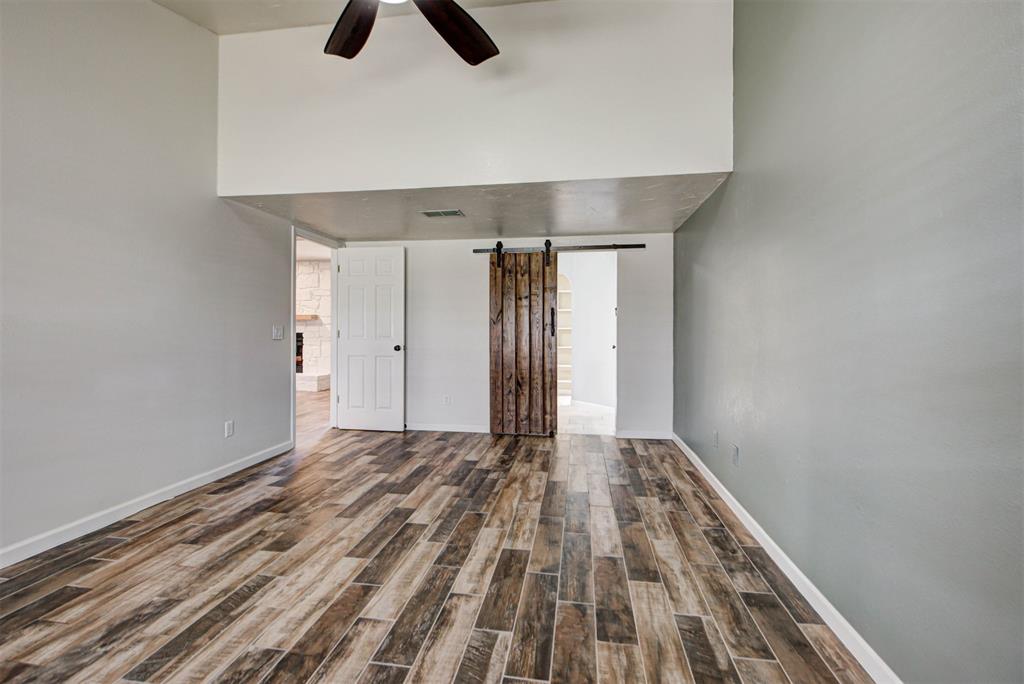 Empty room with wood-look flooring, a ceiling fan, and a rustic sliding barn door.