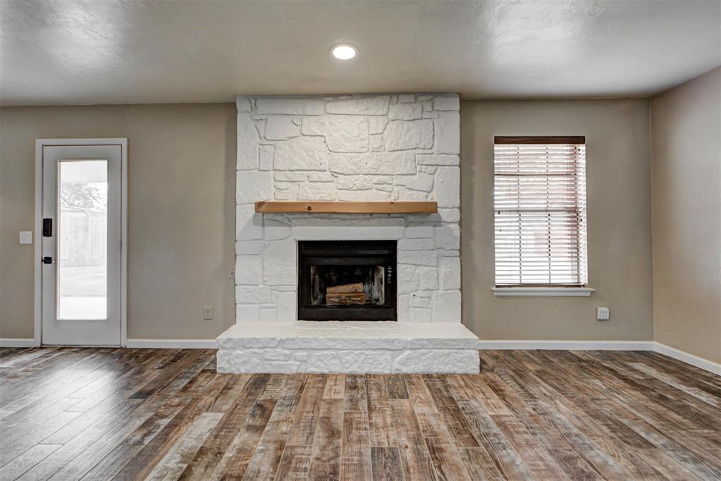 Living room with a large white stone fireplace, wooden mantel, and wood-look plank flooring.