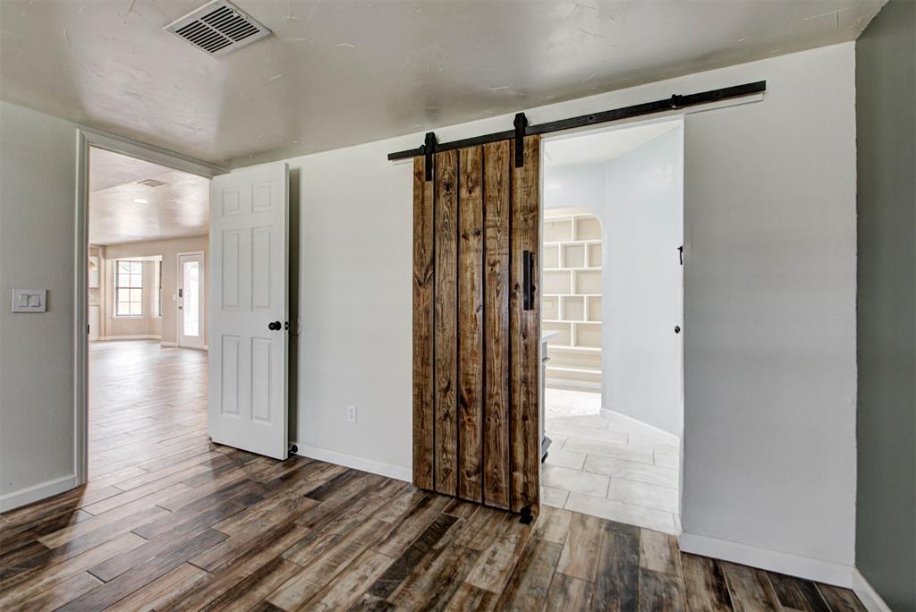 Interior with wood-look flooring, a rustic sliding barn door, and built-in shelving beyond.