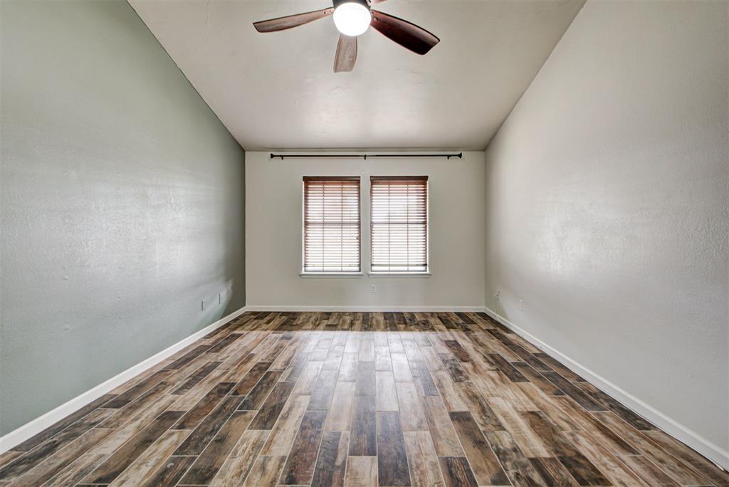 Empty bedroom with wood-look plank flooring, two shaded windows, and a ceiling fan.