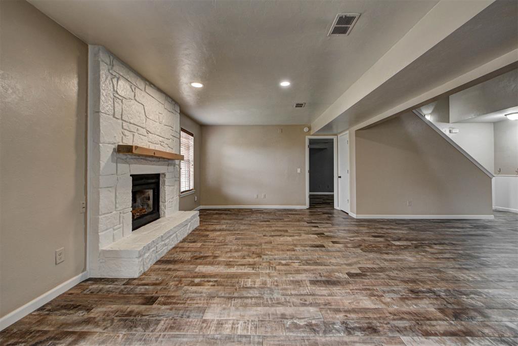 Empty living room with a white stone fireplace and wood-look tile flooring.