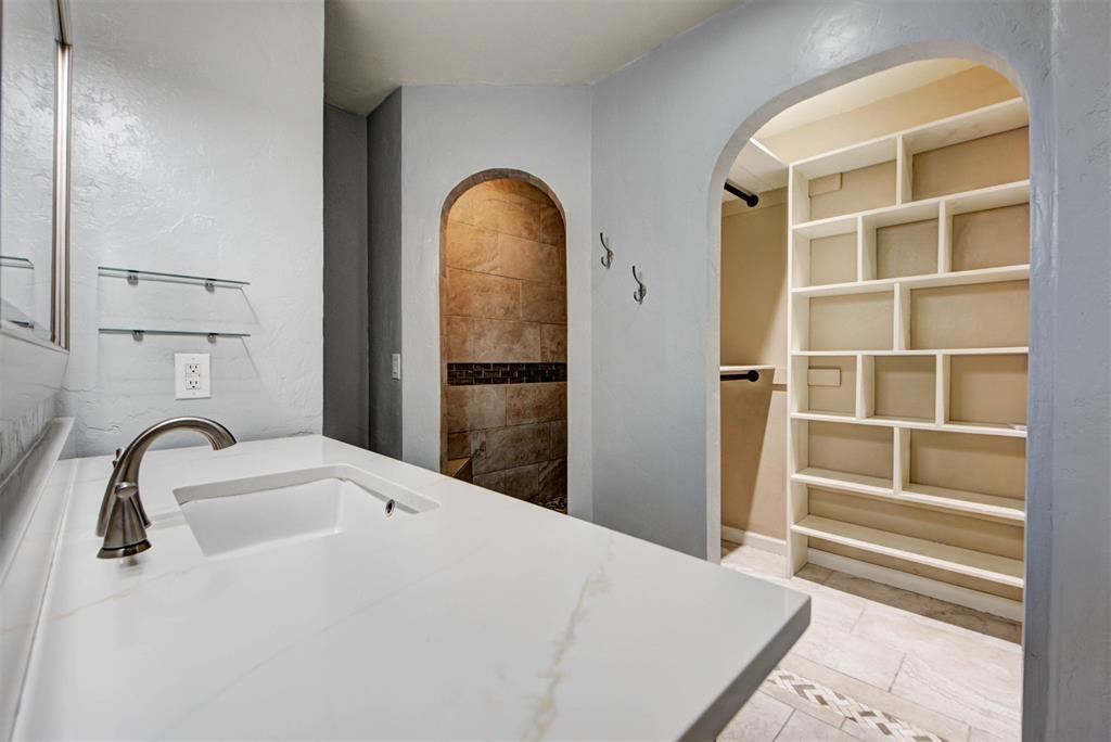 Bathroom with a white vanity, arched tiled shower entrance, and built-in closet shelving.