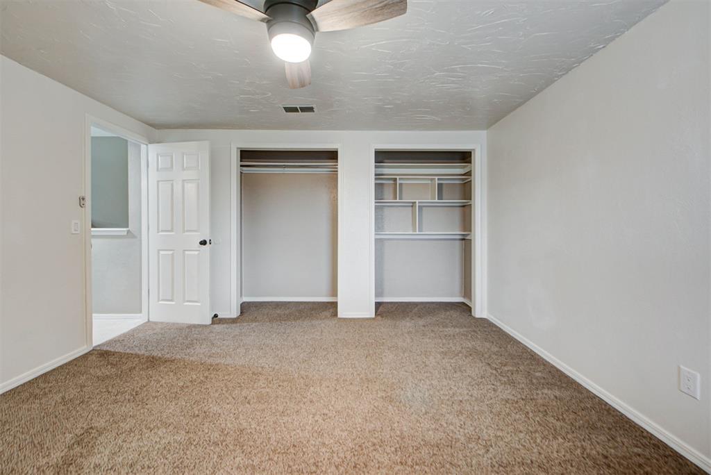 Empty carpeted bedroom with a ceiling fan and two open closets.