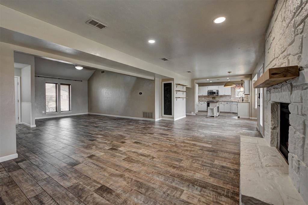 Open living room with wood-look tile floors, a stone fireplace, and kitchen beyond.