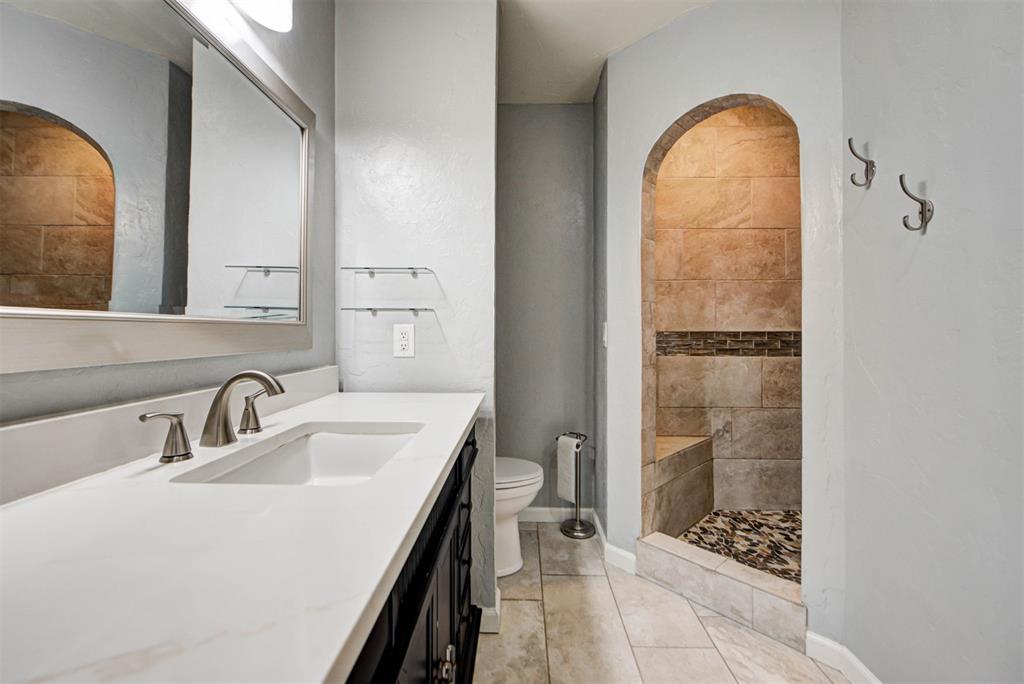 Bathroom with a long white vanity and mirror beside an arched tiled shower.