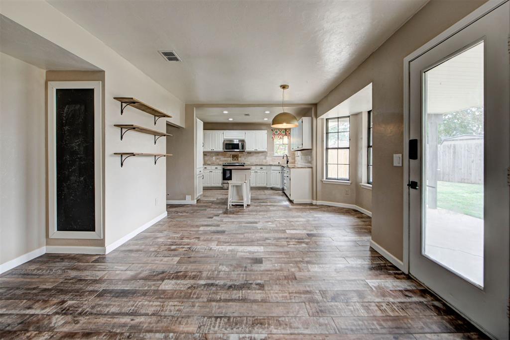 Open living area leading to a white kitchen, with wood-look tile floors and a glass patio door.