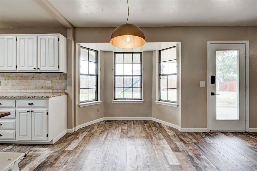 Kitchen and dining area with white cabinets, wood-look flooring, and a bright bay window.