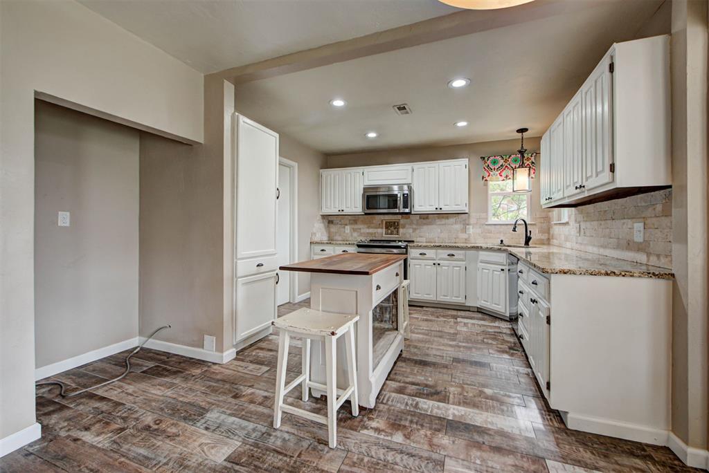 Kitchen with white cabinetry, a central island, tiled backsplash, and wood-look flooring.