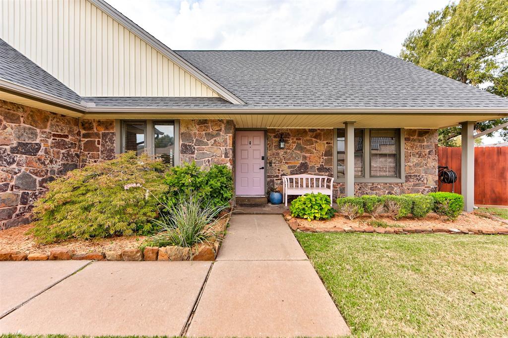Stone-front house with a pink front door, covered porch, and landscaped walkway.