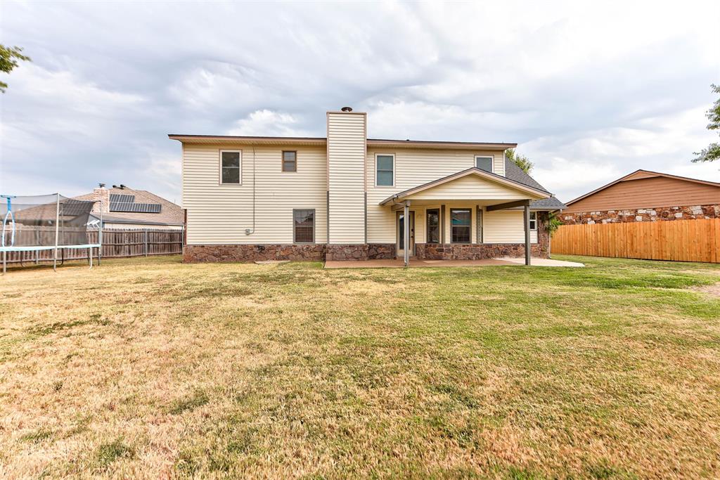Two-story beige house with a covered patio overlooking a fenced backyard and lawn.
