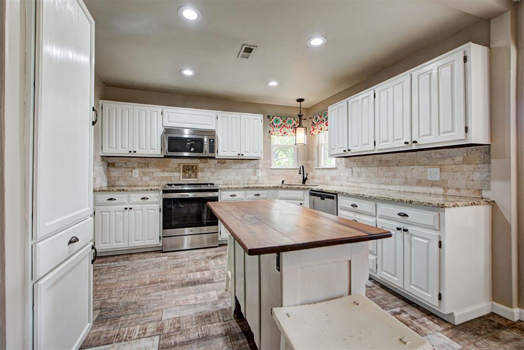 Kitchen with white cabinets, stainless steel appliances, and a large wood-topped island.