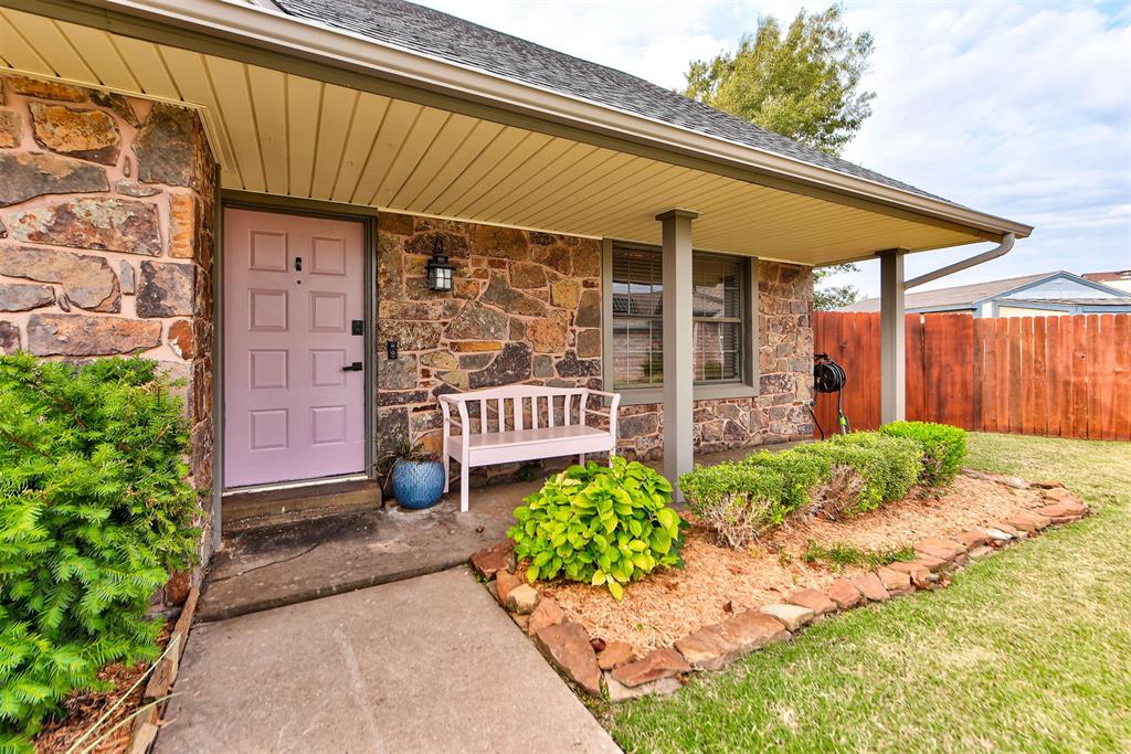 Stone-front home with a covered porch, purple door, white bench, and landscaped entry.