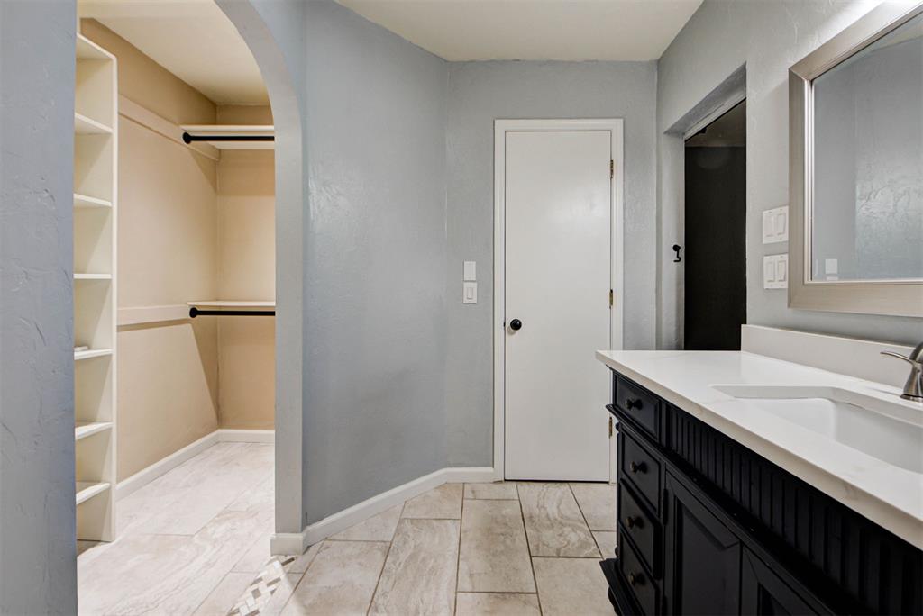 Bathroom with a black vanity and tiled floor beside an open walk-in closet with built-in shelving.
